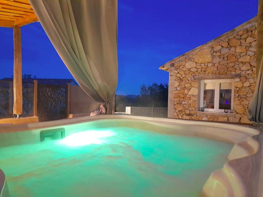 Bain à remous éclairé face à une maison en pierre - L'Antre deux Pierres, romantisme, jacuzzi extérieur, plateau dinatoire