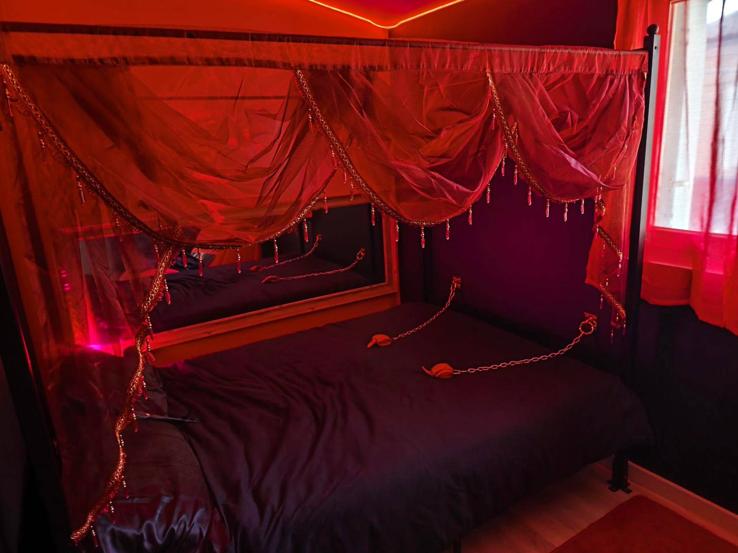 Lit à baldaquin avec voilages rouges et chaînes - Le boudoir des jouissances perverses