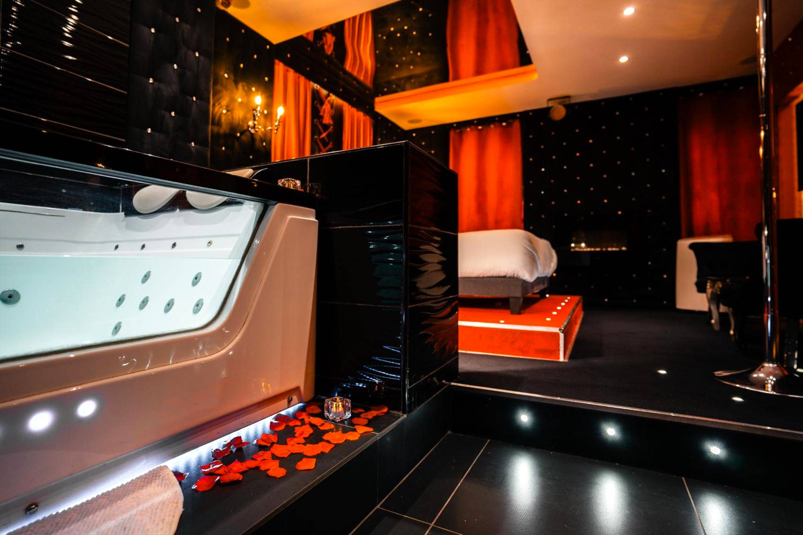 Baignoire balnéo éclairée et lit en arrière - plan - Le Cabaret Vip SPA