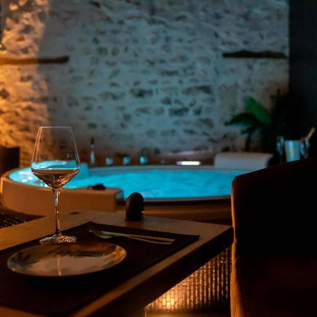 Table dressée face au jacuzzi éclairé en bleu - LOVE Suites & SPA "Le Chai" avec lit rond