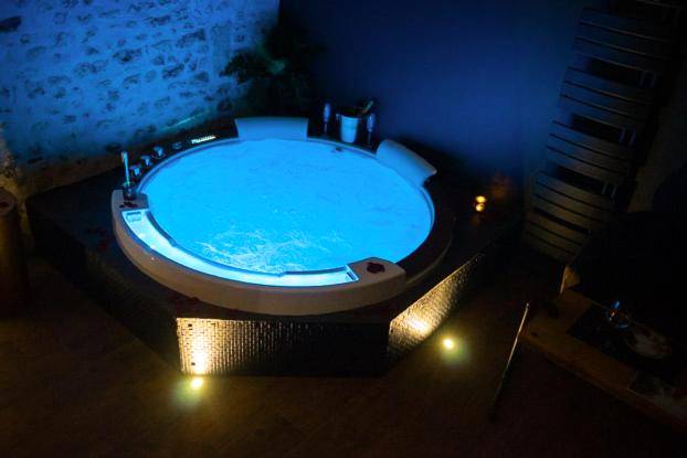 Vue d'ensemble du jacuzzi bleu et mur de pierre - LOVE Suites & SPA "Le Chai" avec lit rond