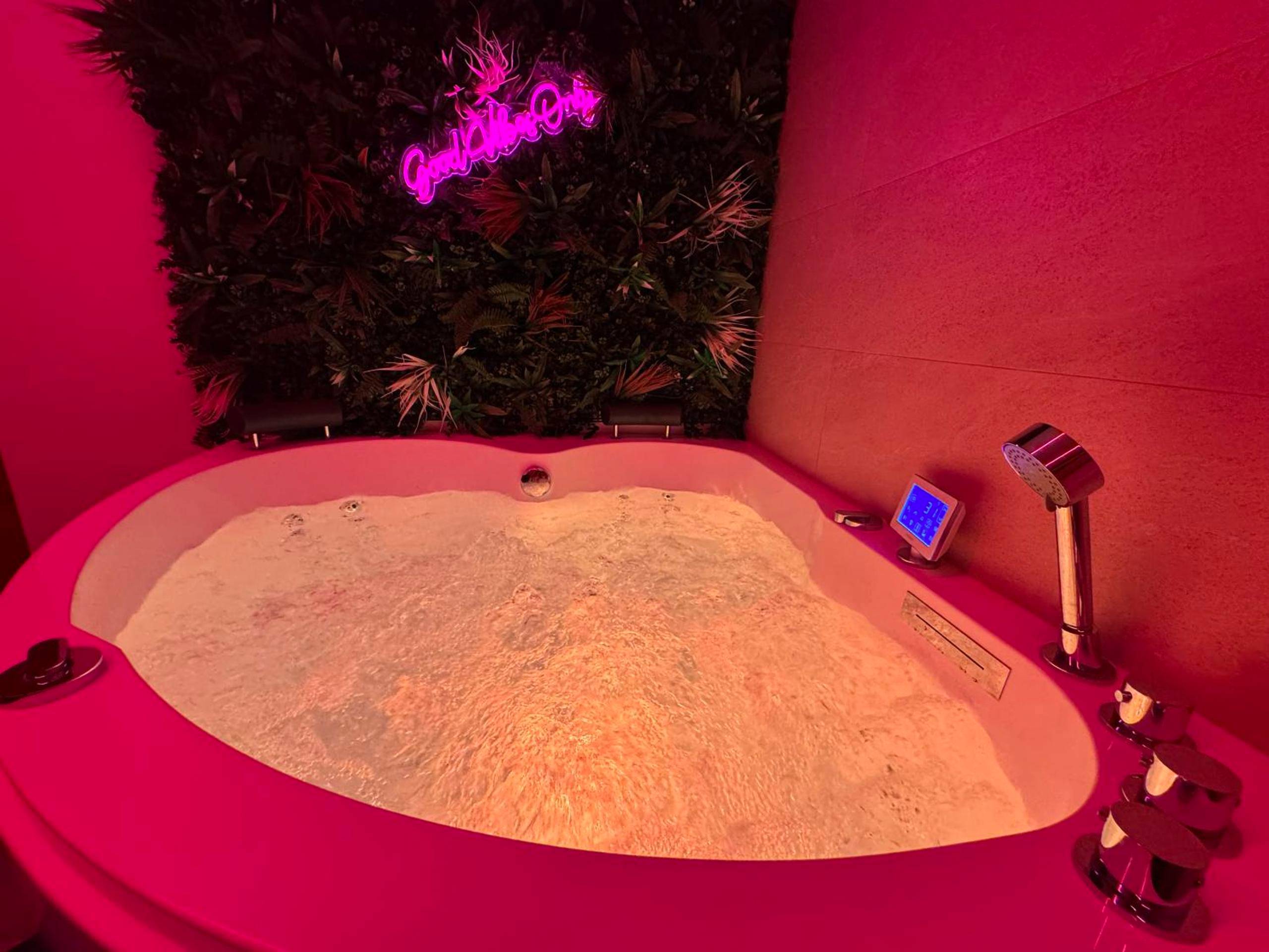Baignoire balnéo sous néon rose et mur végétal - Le Cinéma des Amants