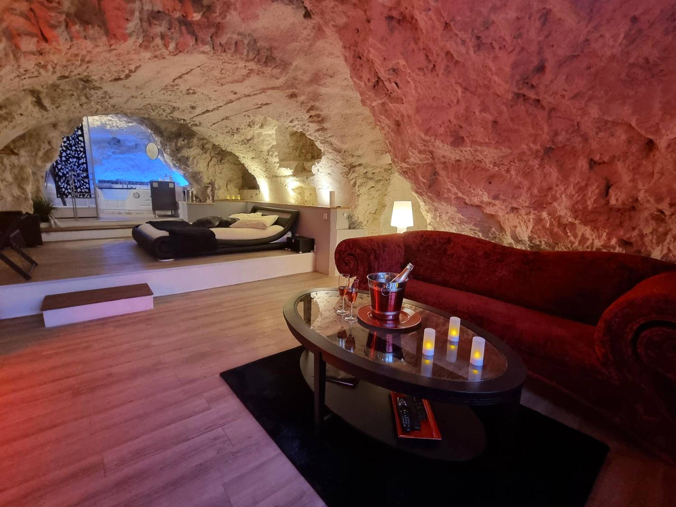 Salon troglodyte avec canapé rouge et lit - Love Room Amboise - Le clos des violettes