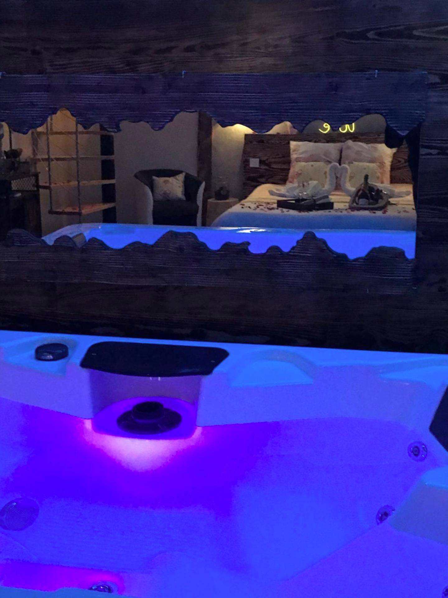 Vue du lit depuis le jacuzzi illuminé - Cosy Love & Spa Love room avec spa, hammam et sauna privatif