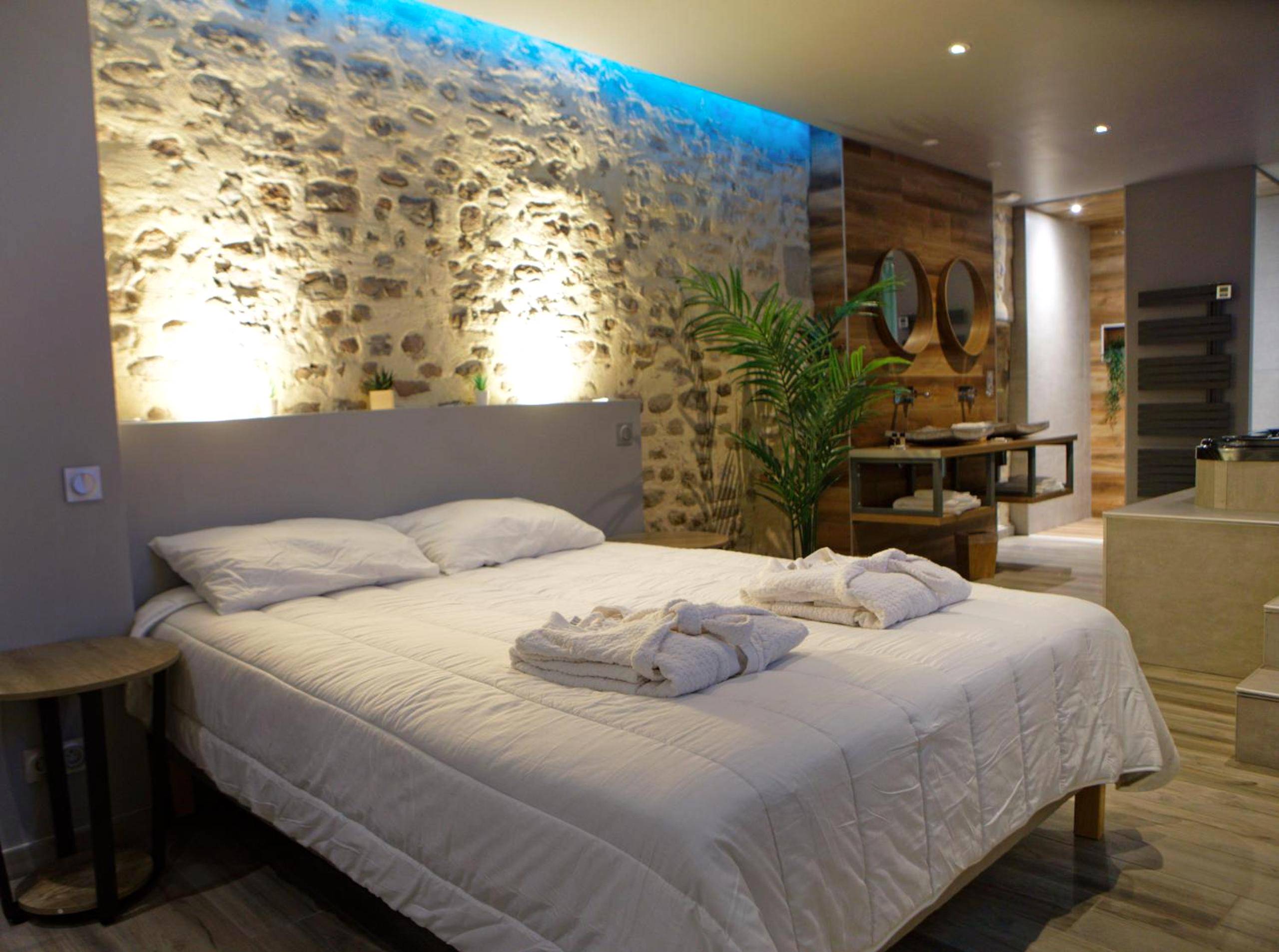Lit double avec peignoirs devant mur en pierre - LA DOLCEVITA SPA Suite privative