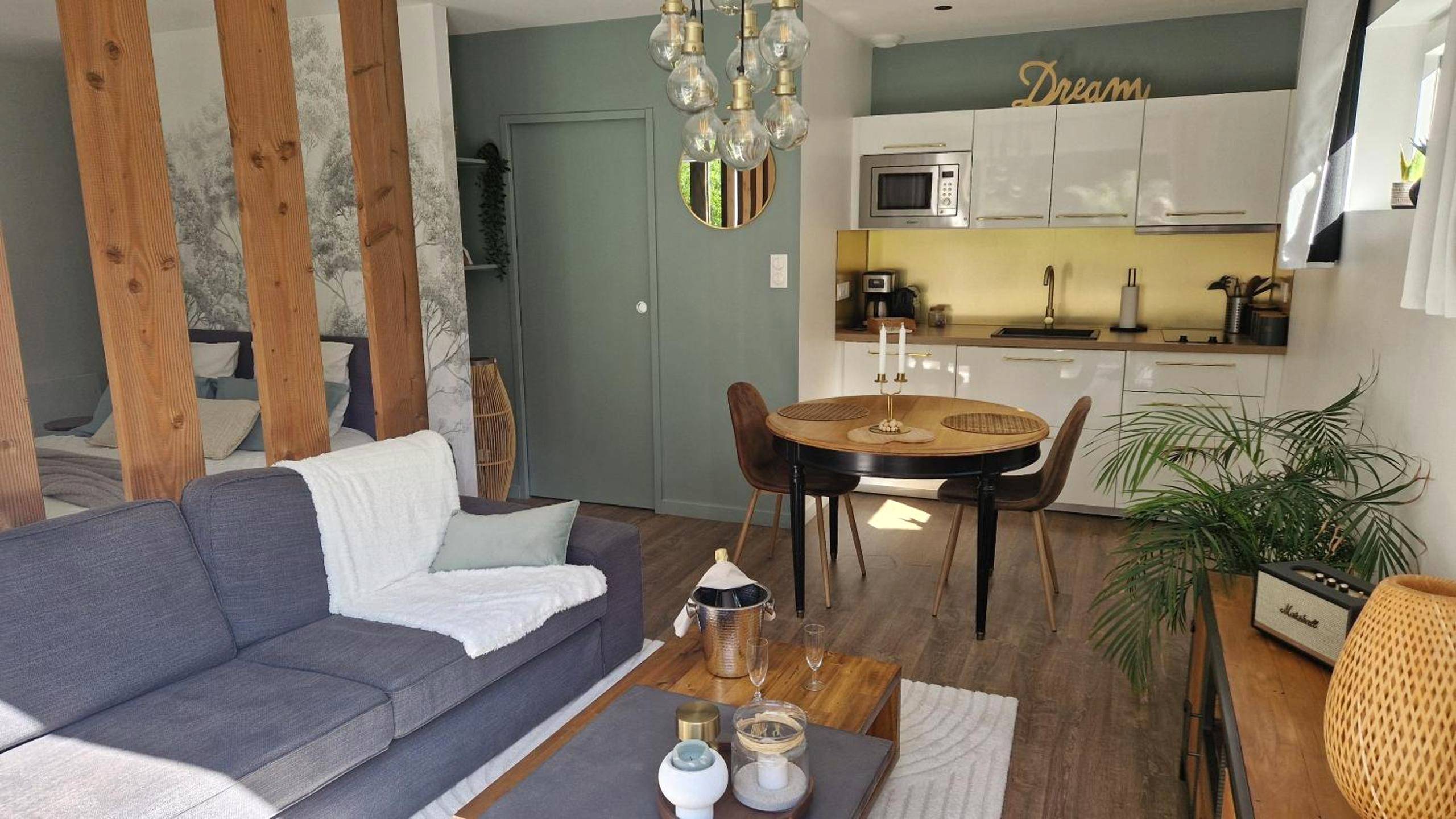 Salon avec canapé gris et coin cuisine équipée - La Douce Escapade