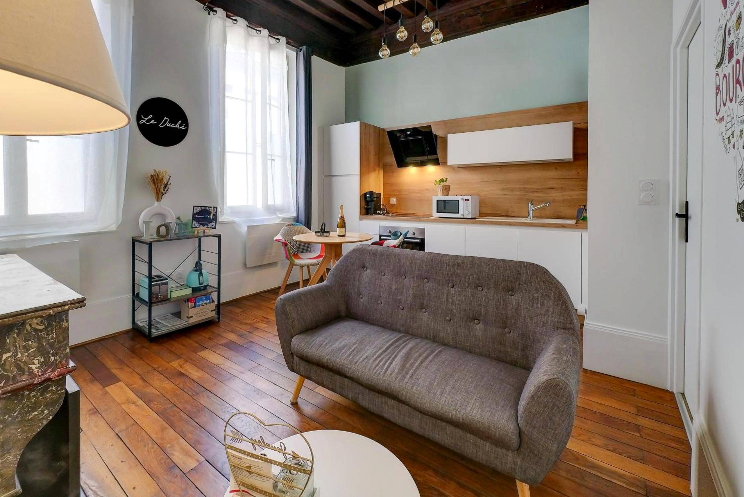 Salon avec canapé gris et cuisine ouverte - Le Duché - Séjour romantique avec balnéo privative - Dijon centre