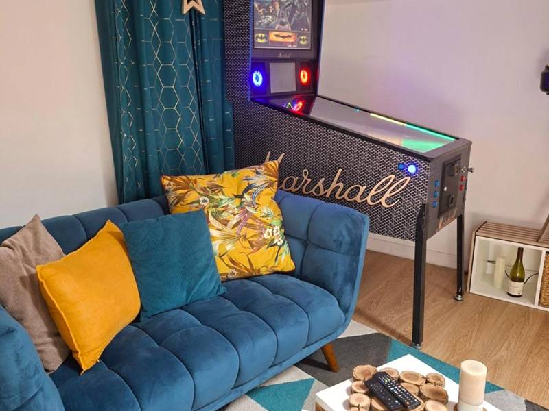 Salon avec canapé bleu et flipper vintage - Nuit Romantique, Spa, Champagne, Cinéma, Flipper - Escapade Veyloise