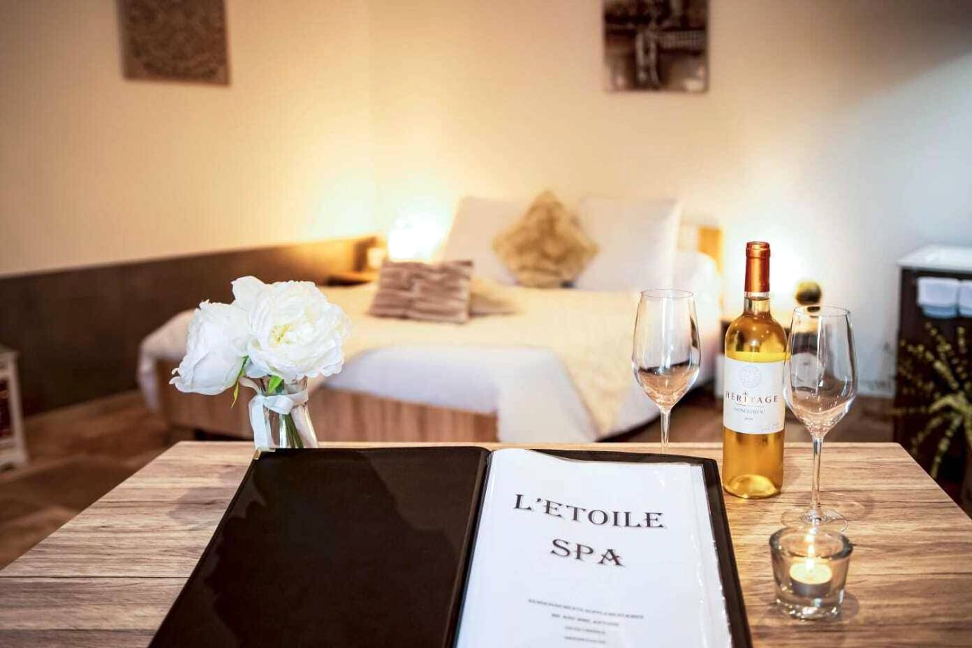 Vin et verres sur table avec lit en arrière - plan - Gites spa de charme L ETOILE SPA