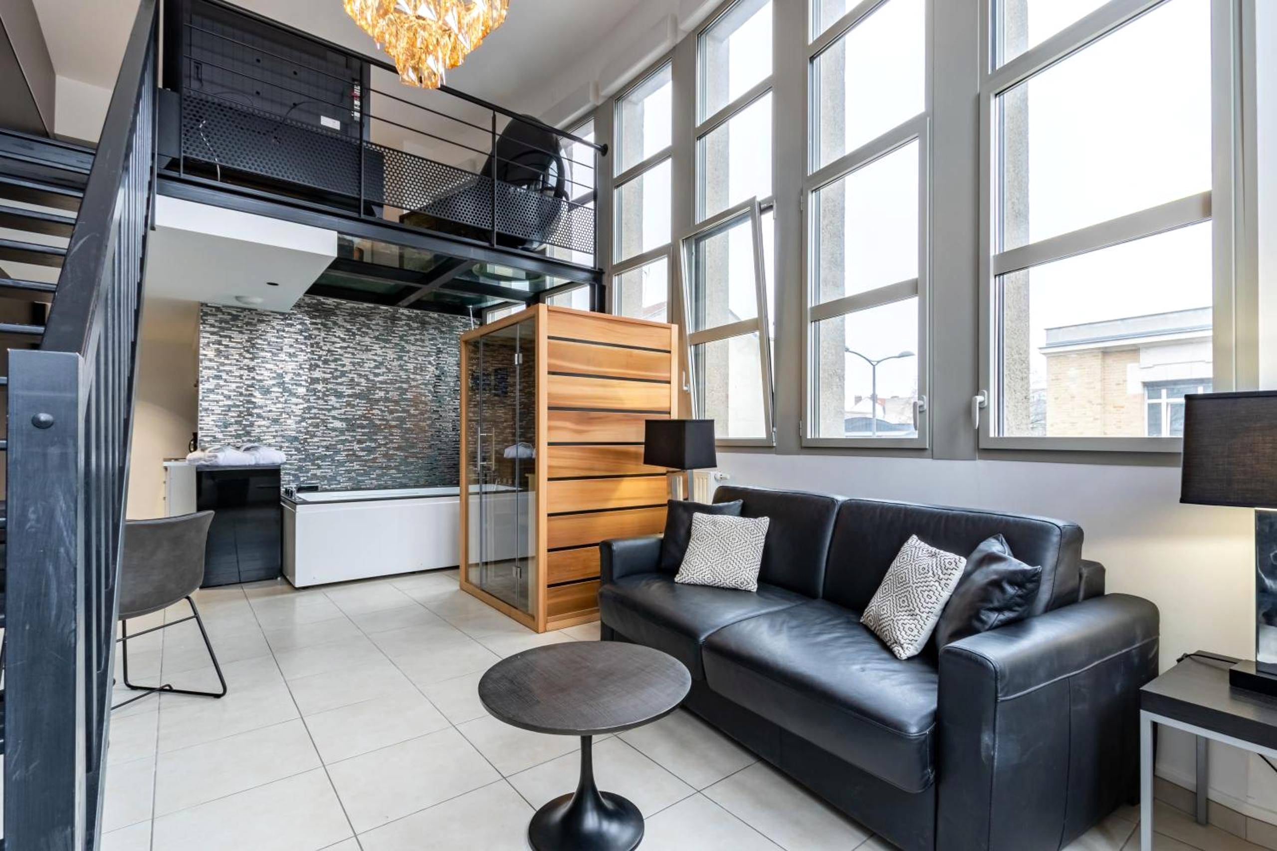 Salon avec canapé noir et sauna en bois - Love Room Reims - GlamappartSpa Prestige New - York expérience