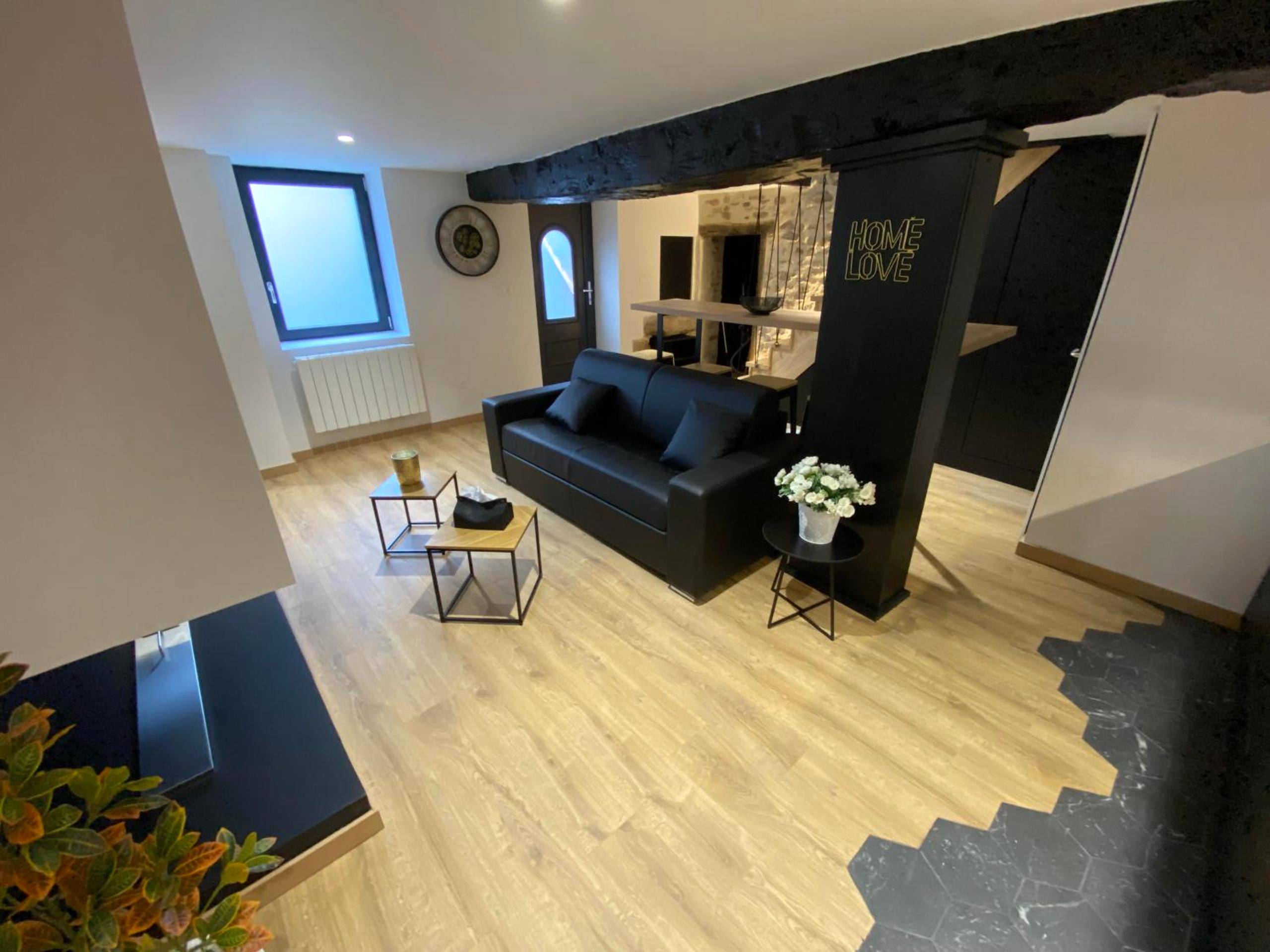 Salon moderne avec canapé noir et parquet - La Home Love location de séduction