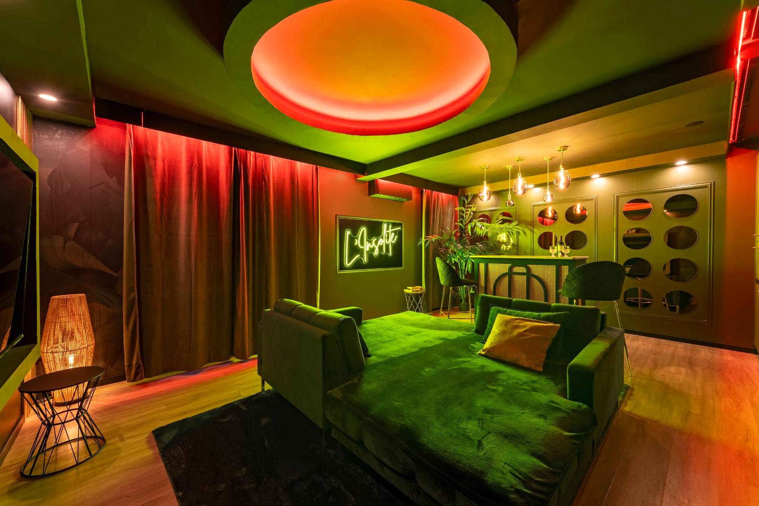 Salon design avec grand canapé vert et néon - L’Insolite, Spa Privatif (Appartement Jacuzzi)
