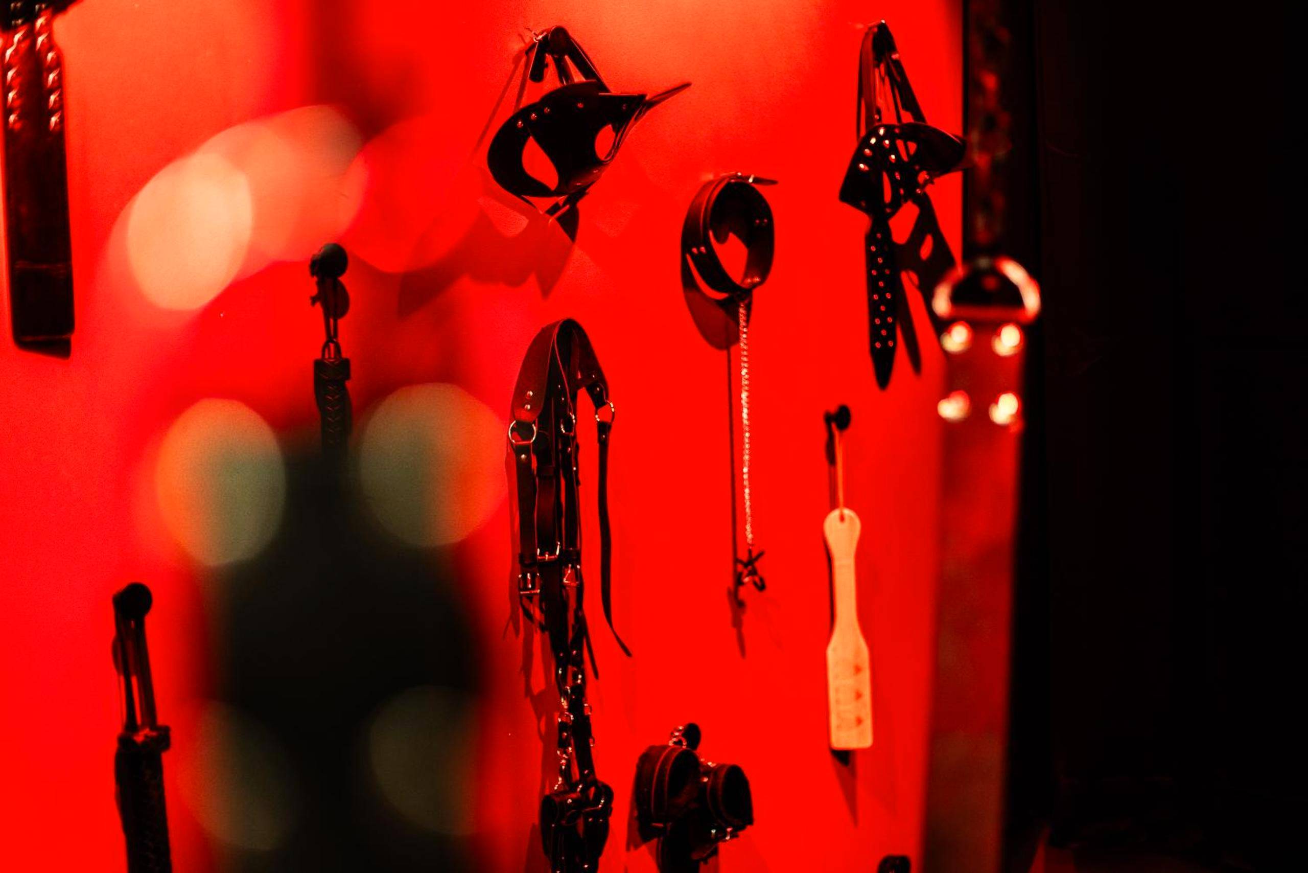 Mur d'accessoires BDSM sur fond rouge - L'instant Secret - Love Room