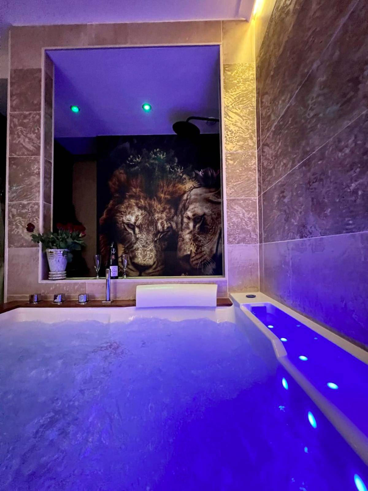 Jacuzzi éclairé en bleu face à fresque lions - Suite KalypsÔ, romantisme, balnéo et sauna privé