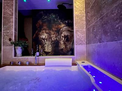 Jacuzzi éclairé en bleu face à fresque lions - Suite KalypsÔ, romantisme, balnéo et sauna privé