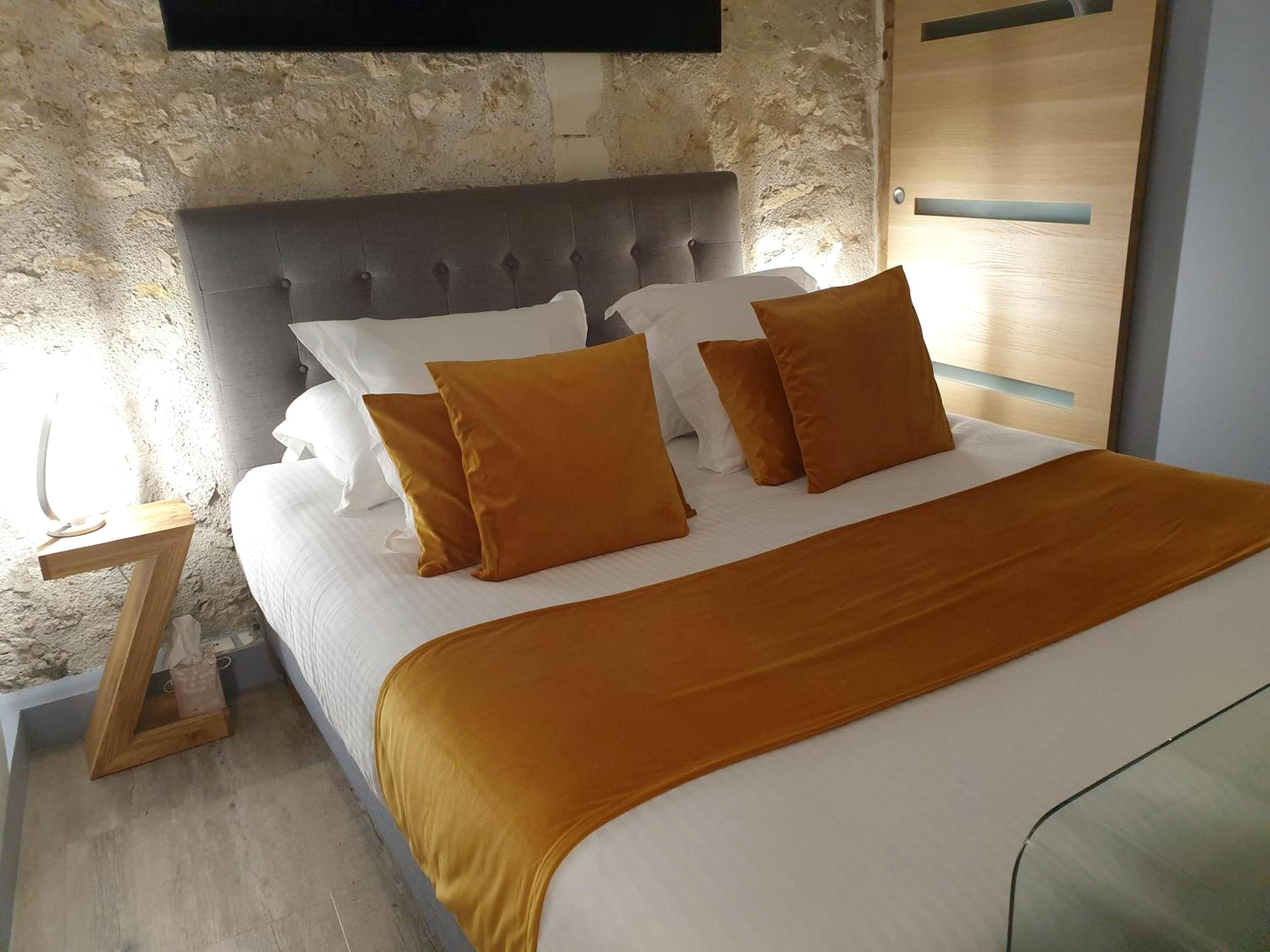 Lit double avec coussins ocre et mur en pierre - Lyzen