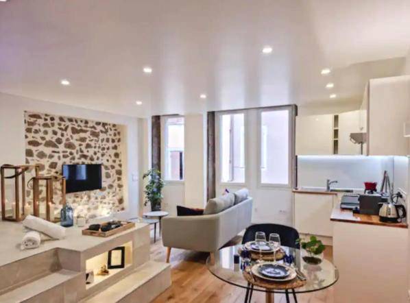 Salon avec mur en pierre et cuisine équipée - Majord'Home Spa 5* - La Source Cœur Vieille Ville