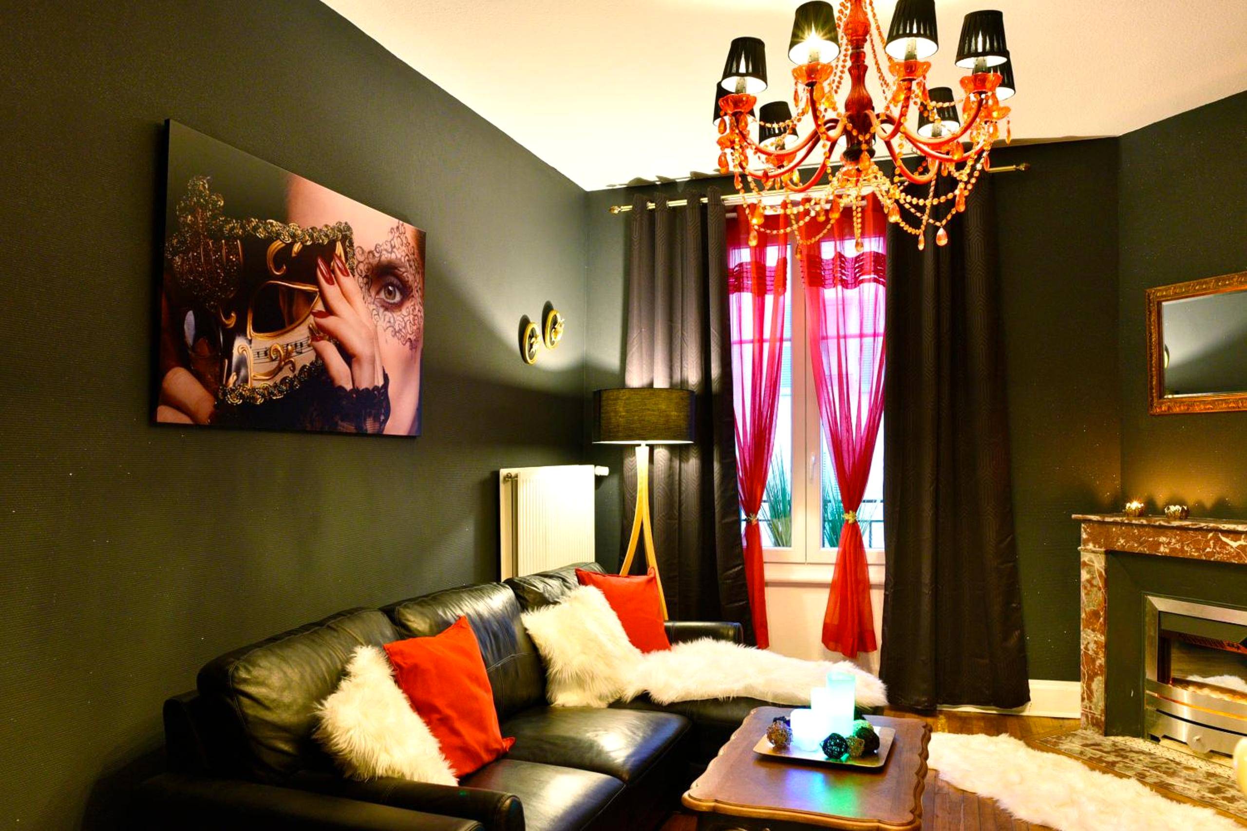 Salon avec canapé en cuir et lustre rouge - MoonLOVE, SPA/Sauna et Jacuzzi privés, charme et détente.