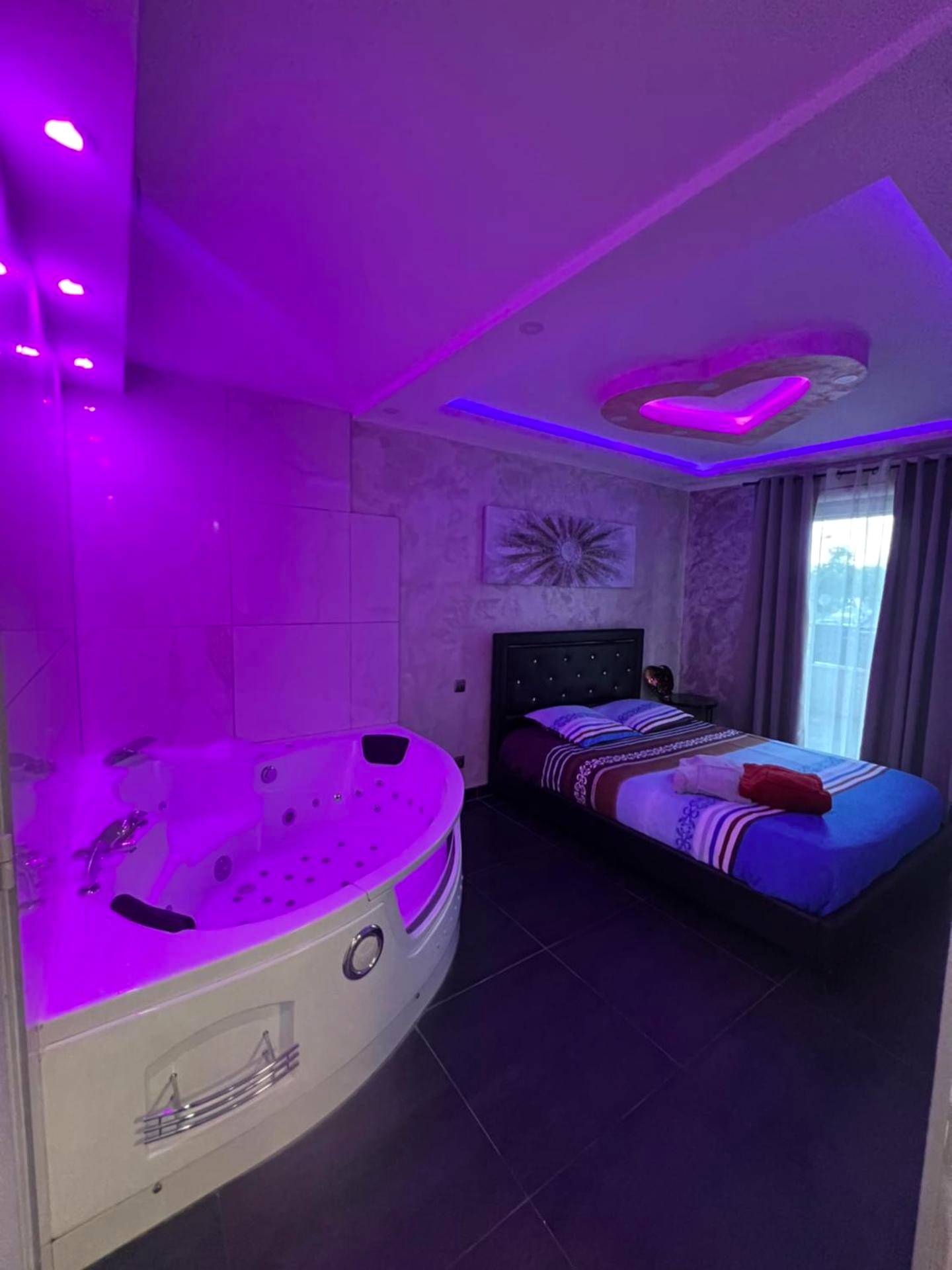 Baignoire balnéo et lit double sous néons roses - Nid d'Amour