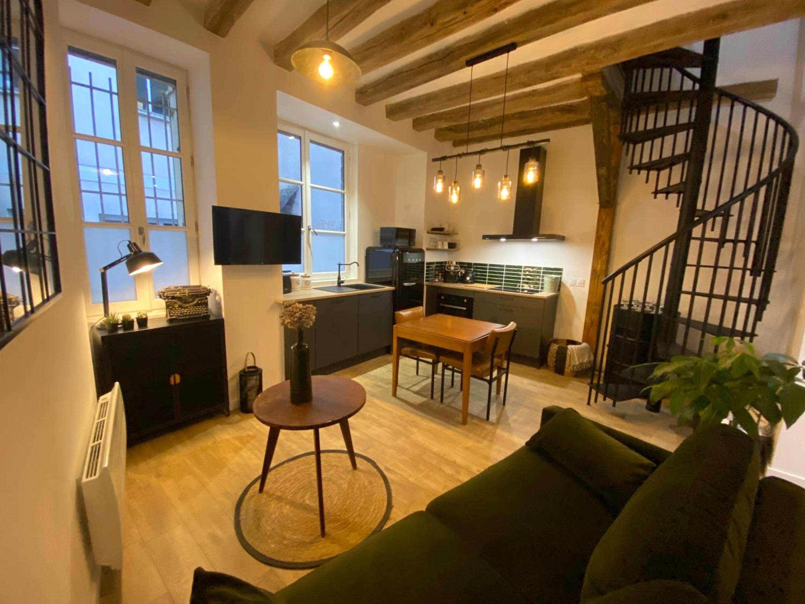 Salon avec canapé vert et poutres apparentes - L'Oasis Angevine - Balneo, Sauna, Home Cinema & Parking