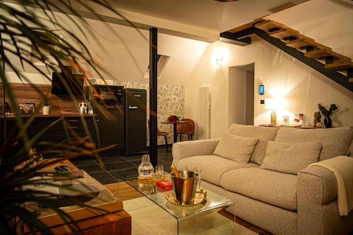 Salon avec canapé gris et coin cuisine équipée - La Parenthèse Suites - appartement luxueux avec sauna et baignoire balnéo