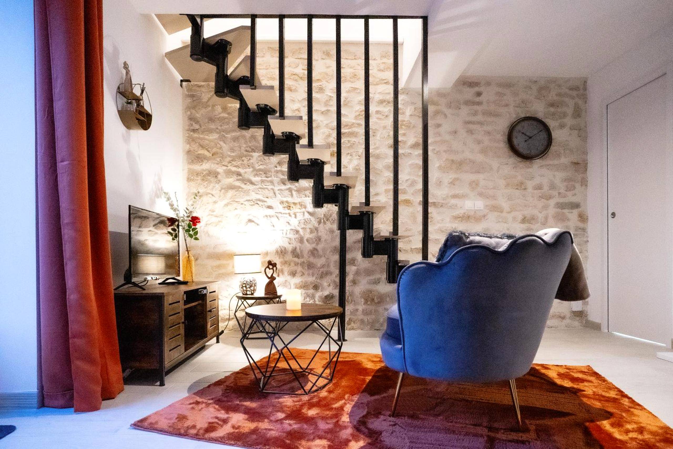 Salon avec fauteuil bleu et mur en pierre - Love Room Château - Landon - Love Room Une Pause à Deux - Jacuzzi - Chambre...