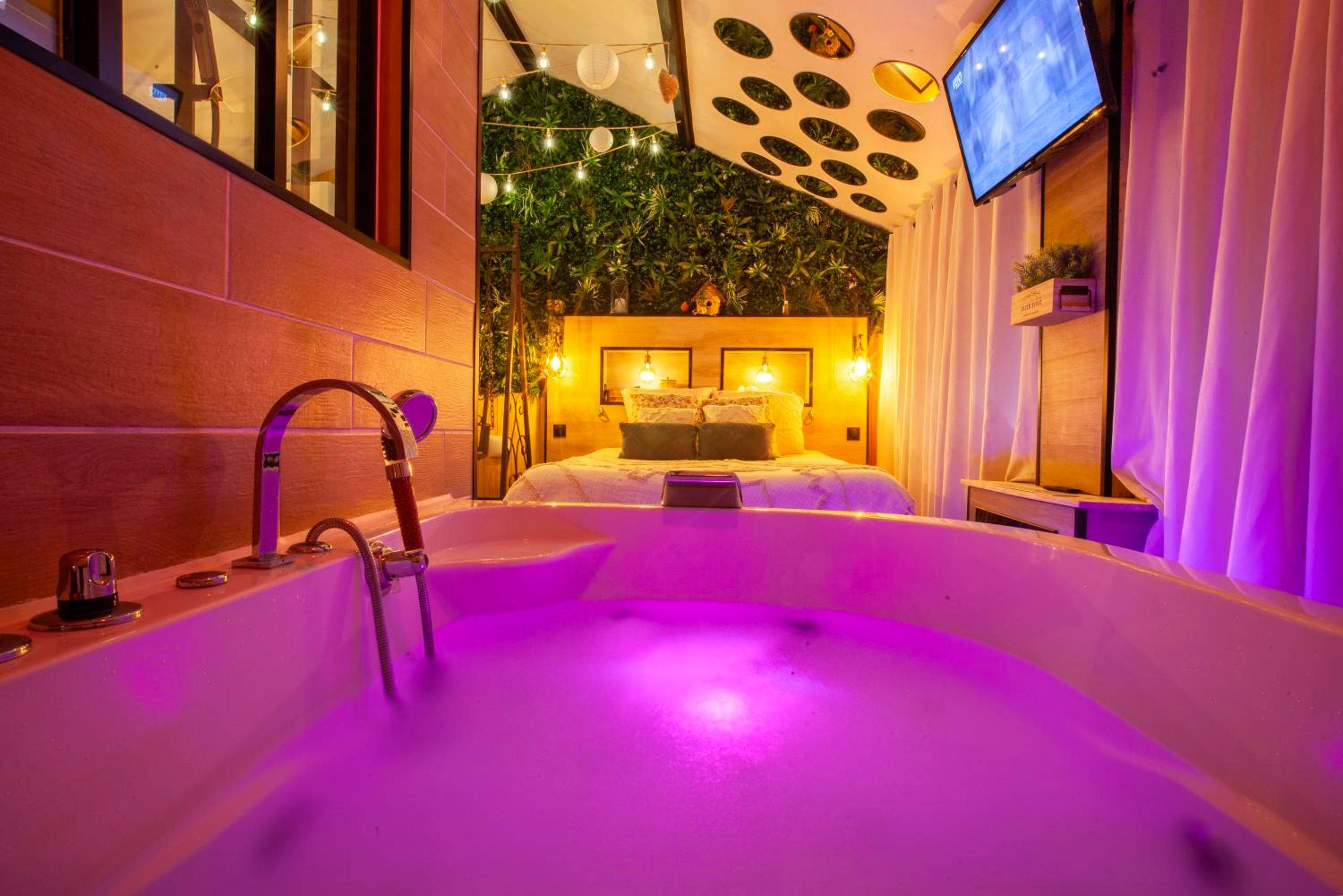 Jacuzzi privatif avec éclairage rose et lit - Love Room Angers - Love Room Romantique Les Petits Plaisirs