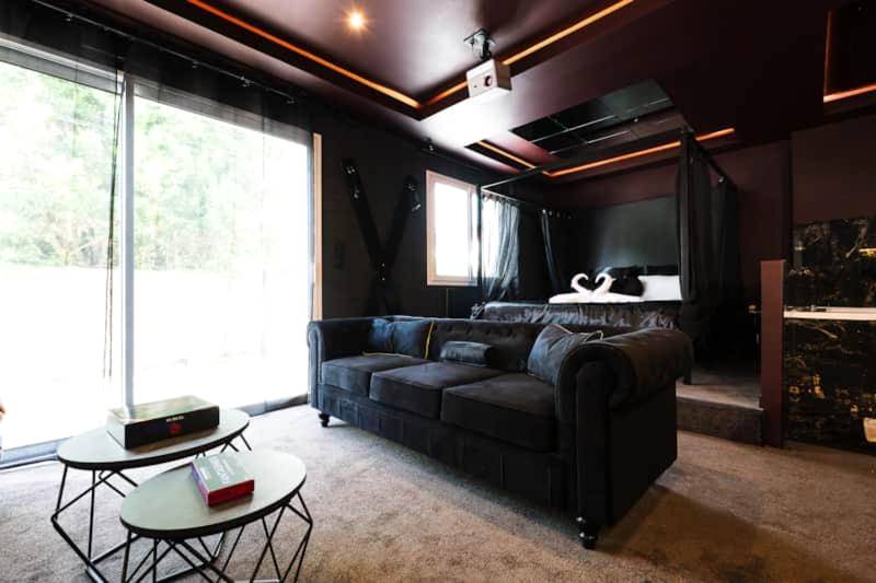 Salon avec canapé noir et lit à baldaquin - Promesse d'une nuit avec Balnéo privative
