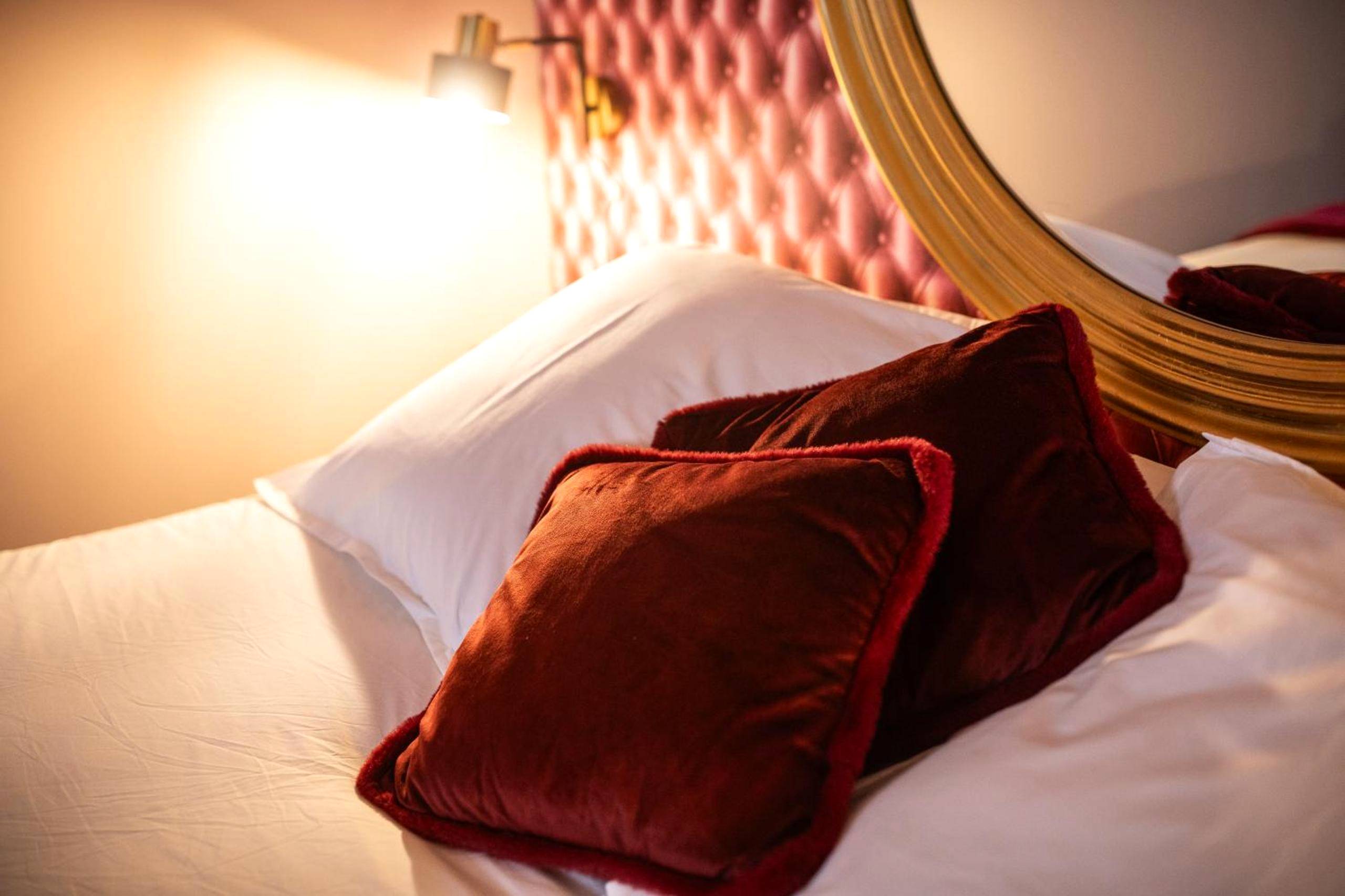 Détail des coussins en velours rouge sur le lit - Reflet des sens Love & Balnéo