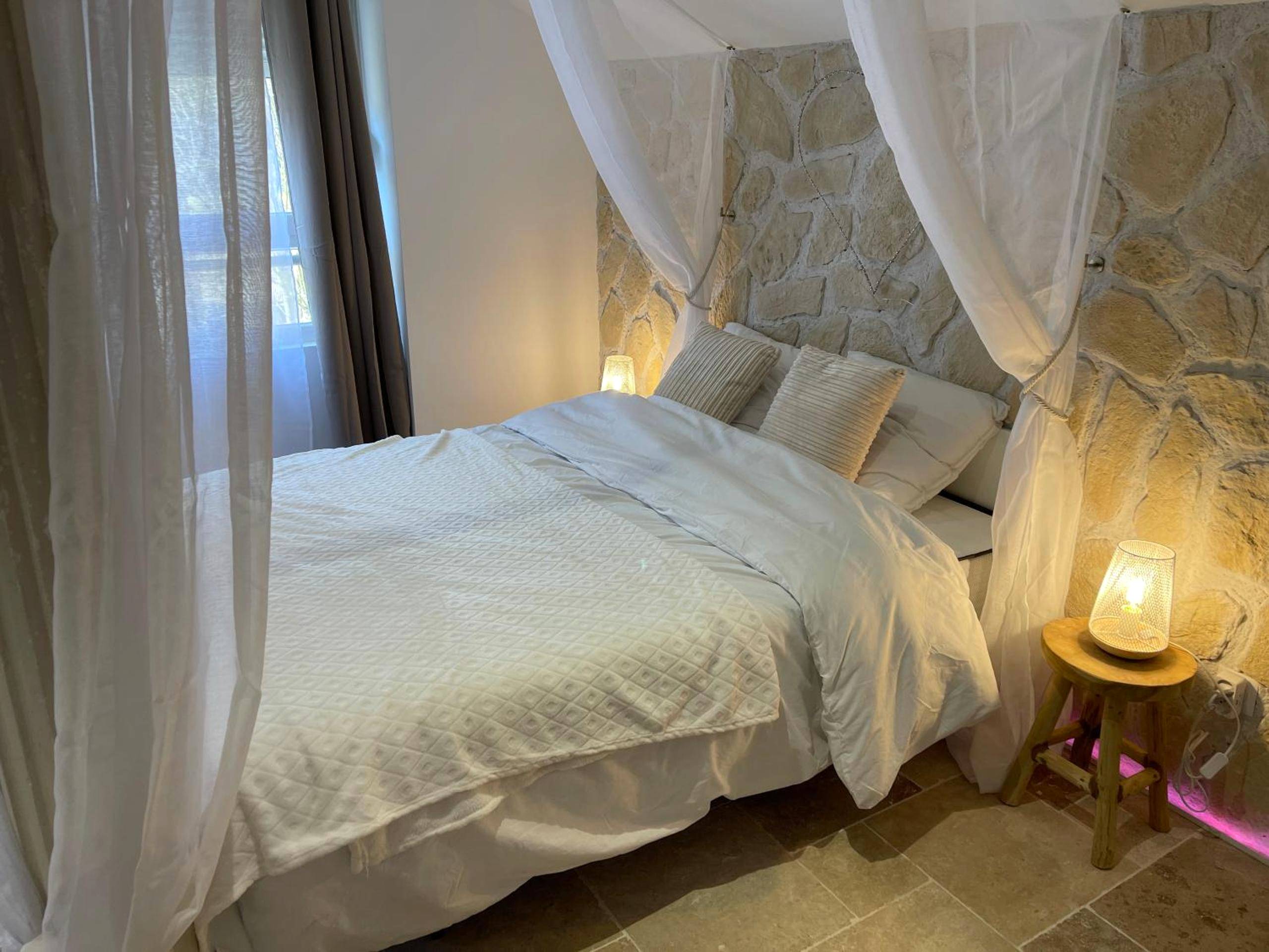 Lit double avec voilages et mur en pierre - Romantica Spa
