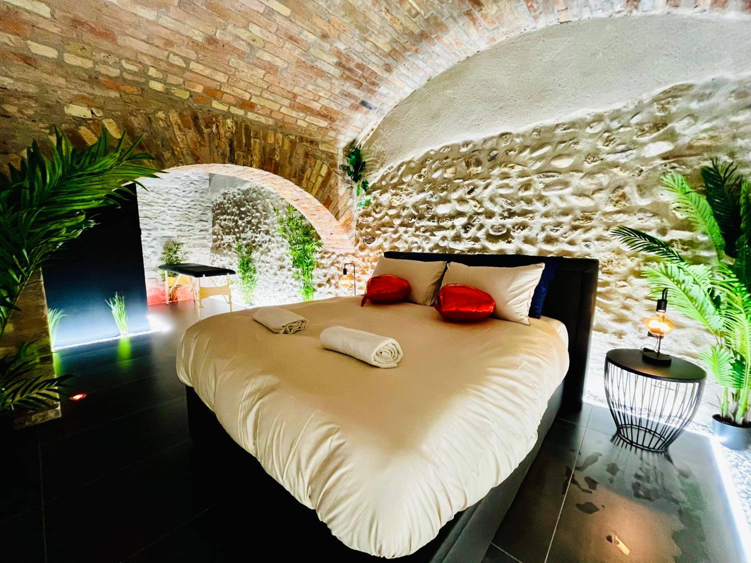 Lit double avec coussins cœurs et mur en pierre - Le Secret de Valence