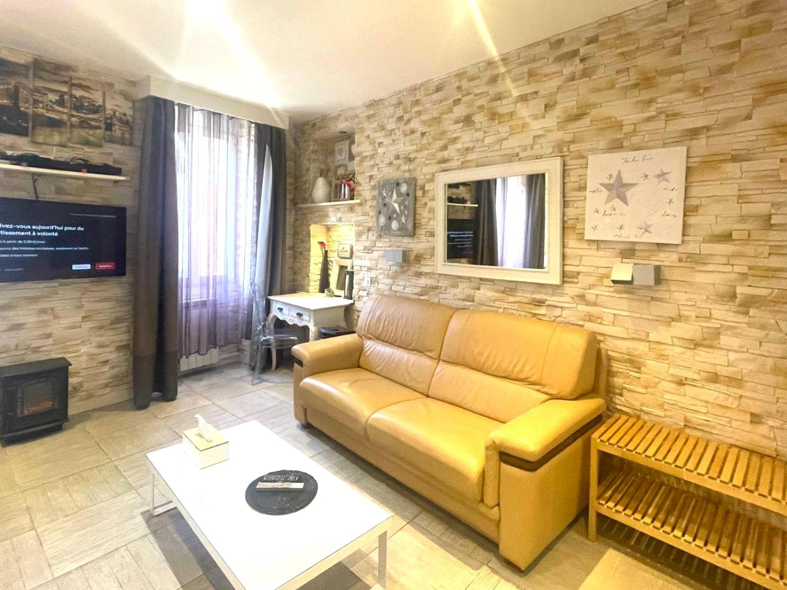Salon avec canapé en cuir et mur en pierre - Appart' Spa et Sauna Privatif Au Cœur De Beaune