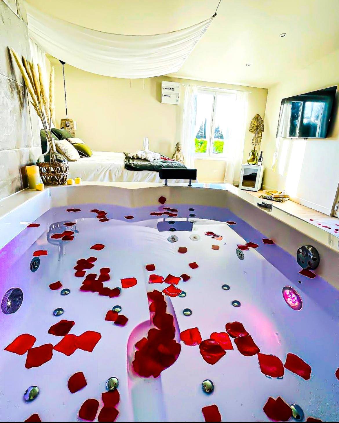 Jacuzzi avec pétales de rose et lit en arrière - Love Room Sorgues - Suite évasion au cœur des vignes