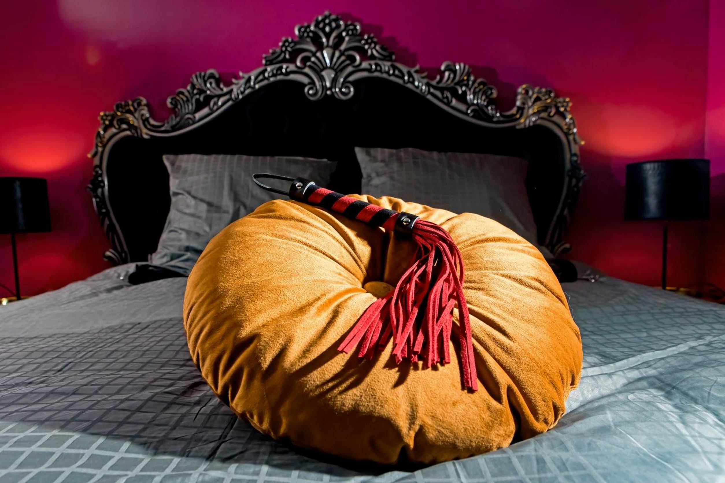 Fouet posé sur coussin rond devant tête de lit - SUITE PLAYROOM Love Hotel Toulouse