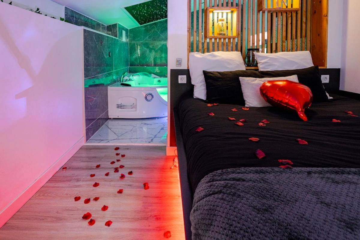 Lit avec pétales de rose et jacuzzi en fond - Suite romantique Spa Balnéothérapie