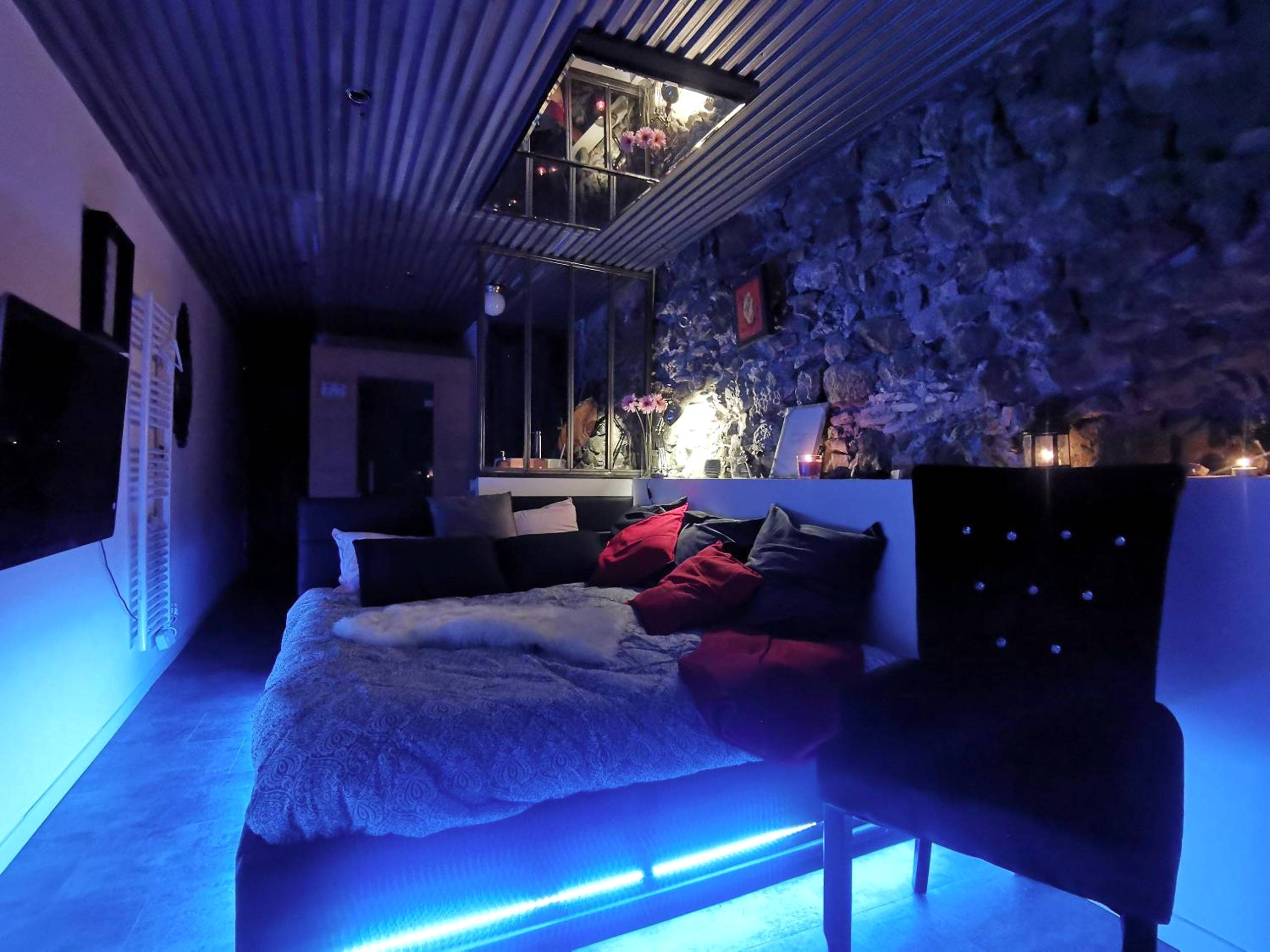 Chambre avec éclairage LED bleu et mur de pierre - Sweet Loft Grenoble - Love Room avec jacuzzi & sauna
