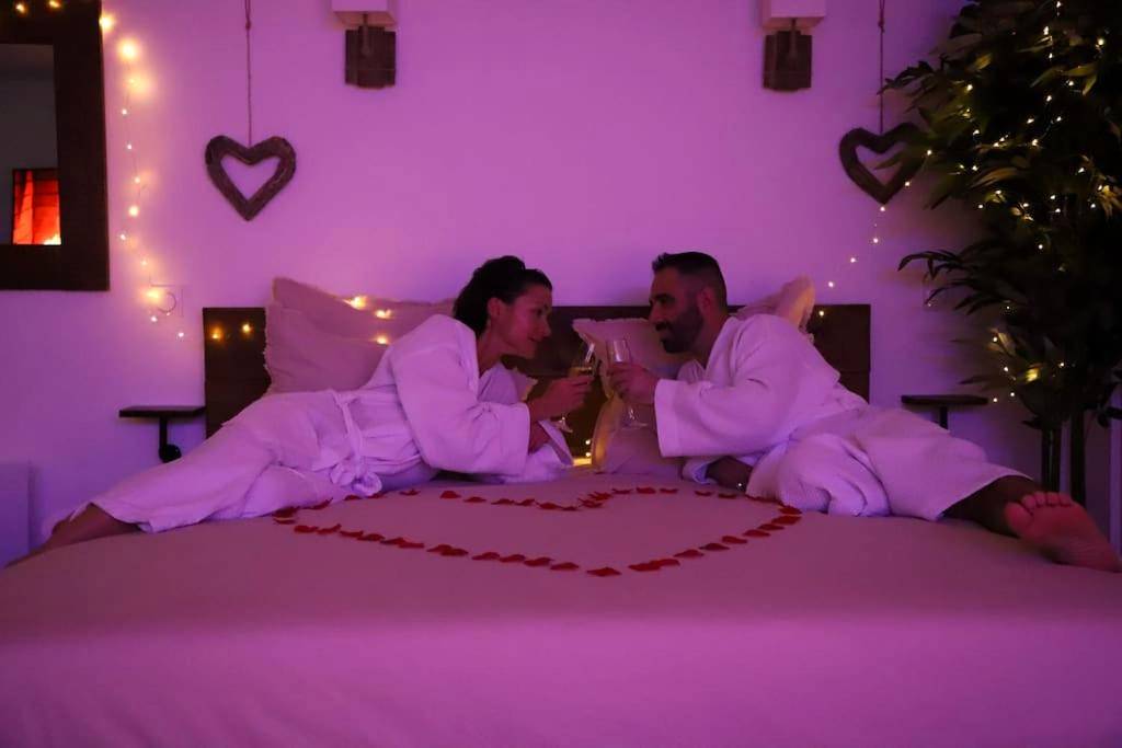 Couple trinquant sur lit parsemé de pétales - Love Room Charleville - Mézières - Love room Unique - Sauna / Jacuzzi