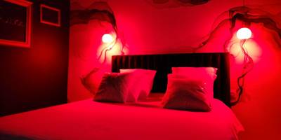 Lit double sous lumière d'ambiance rouge - La Volupté - Love room avec Jacuzzi - Sauna